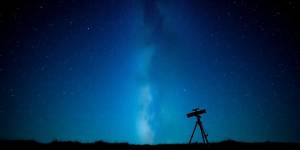 Telescope under a starry night sky with Milky Way.