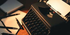 Close-up of a typewriter with scattered writing tools.