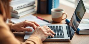 Person typing on laptop with books and papers.