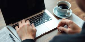 Journalist typing on a laptop with notes and coffee.