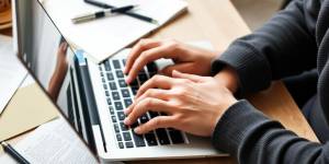 Person typing on a laptop with notes and coffee.